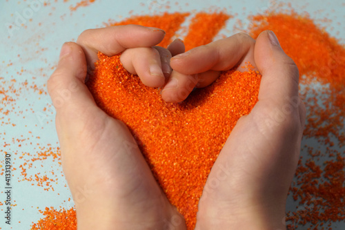 Fotografie, Obraz sand therapy, orange kinetic sand in the shape of a heart in children's hands