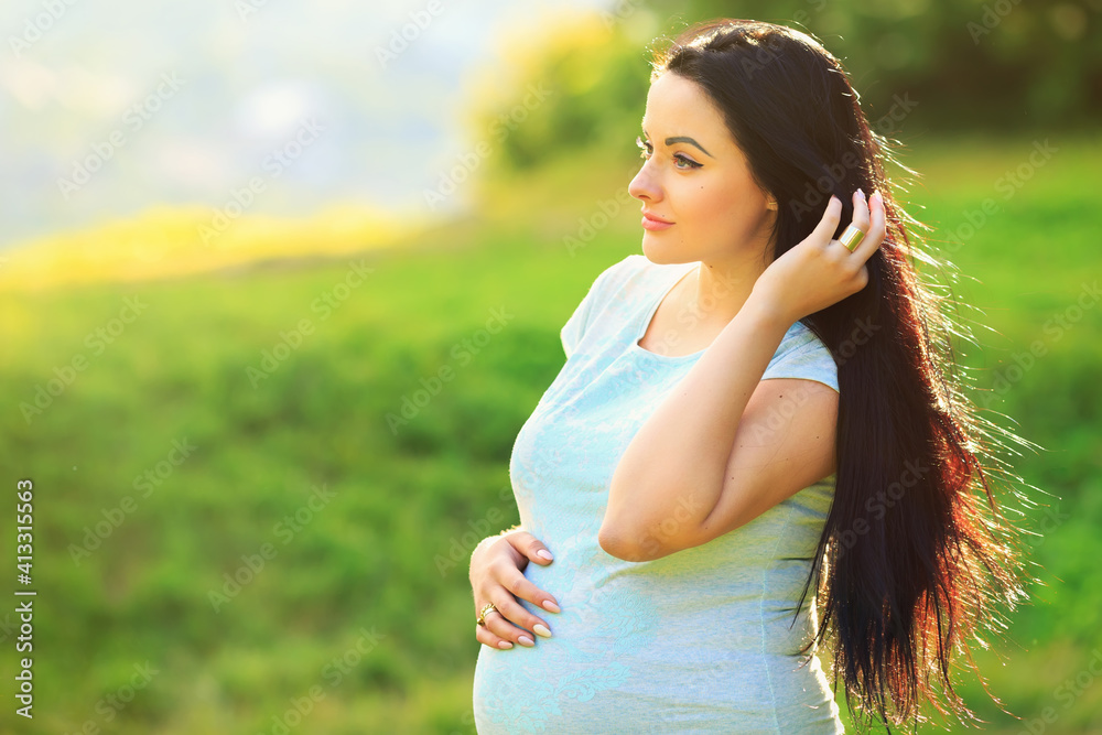 Beautiful pregnant woman feels great to relax in the park. Dressed in casual clothes. Looks to the side straightens her hair. Beautiful pregnant woman feels great to relax in the park. Dressed in casual clothes. Looks to the side straightens her hair.