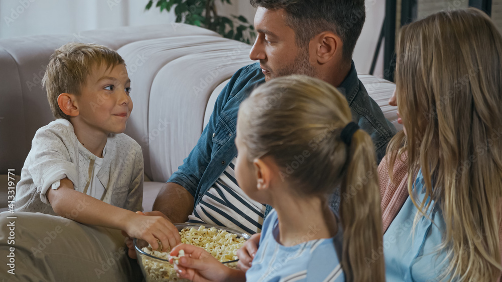 Boy taking popcorn near family on blurred foreground at home