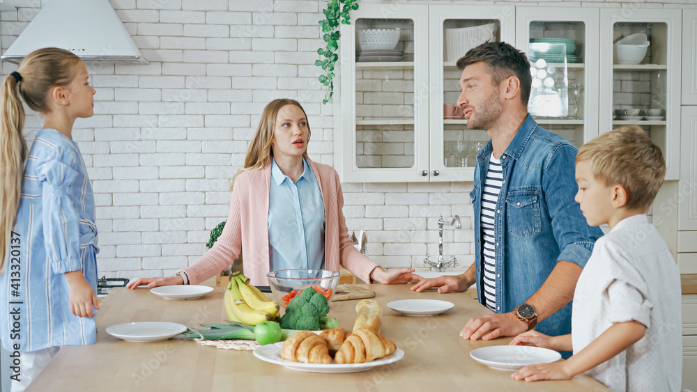 Family with kids talking near food and plates on kitchen table