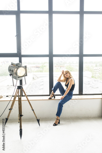 young beautiful blonde girl in a black T-shirt and blue pants sits near the window