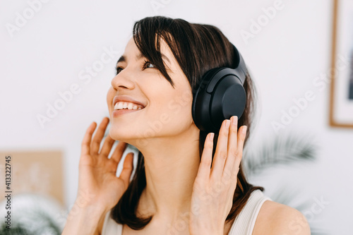 Closeup portrait of a happy young woman smiling, listening to music in wireless headphones.