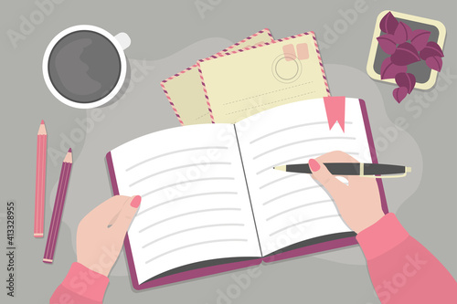 Female hand holds pen and writes down notes. Top view of desktop. Desk with pencils and cup of coffee