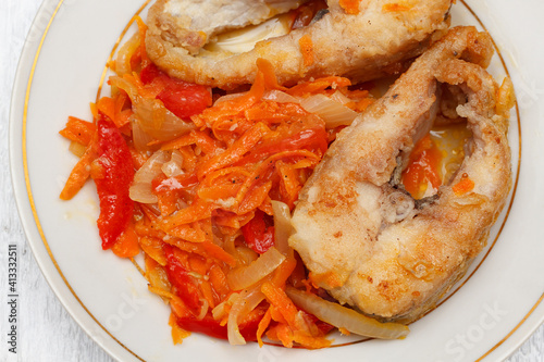 Pieces of fried pike with a vegetable garnish of bell peppers, onions and carrots on a round white plate.