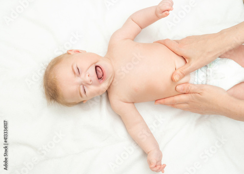 Newborn is crying because of colic pain. Massage stomach for little newborn baby. Mom massaging colic tummy of newborn