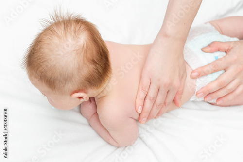 Three month baby boy receiving back massage from a female massage therapist. Relaxing newborn kid. Close up. The masseur gives the child a back massage