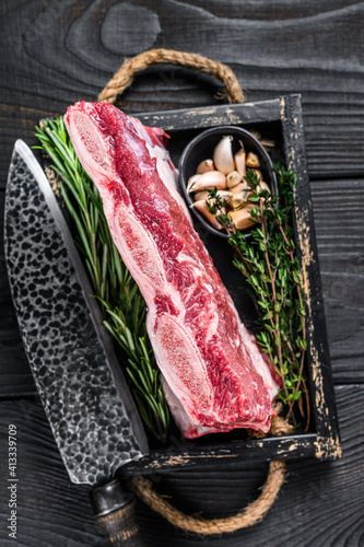 Fresh Raw veal short ribs in a wooden tray with herbs. Black wooden background. Top view