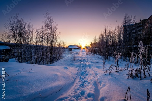 Evening winter landscape with a path leading to the horizon with the setting sun. Frosty trees