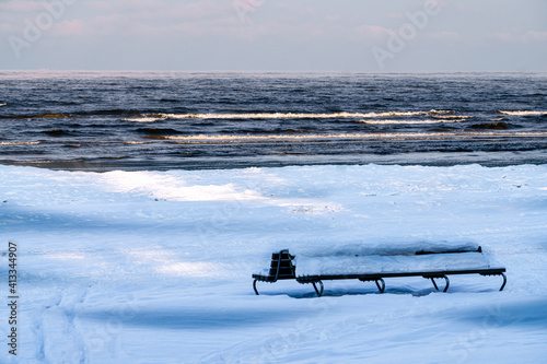 A snow-covered bench on a snow-covered beach in the Gulf of Riga.