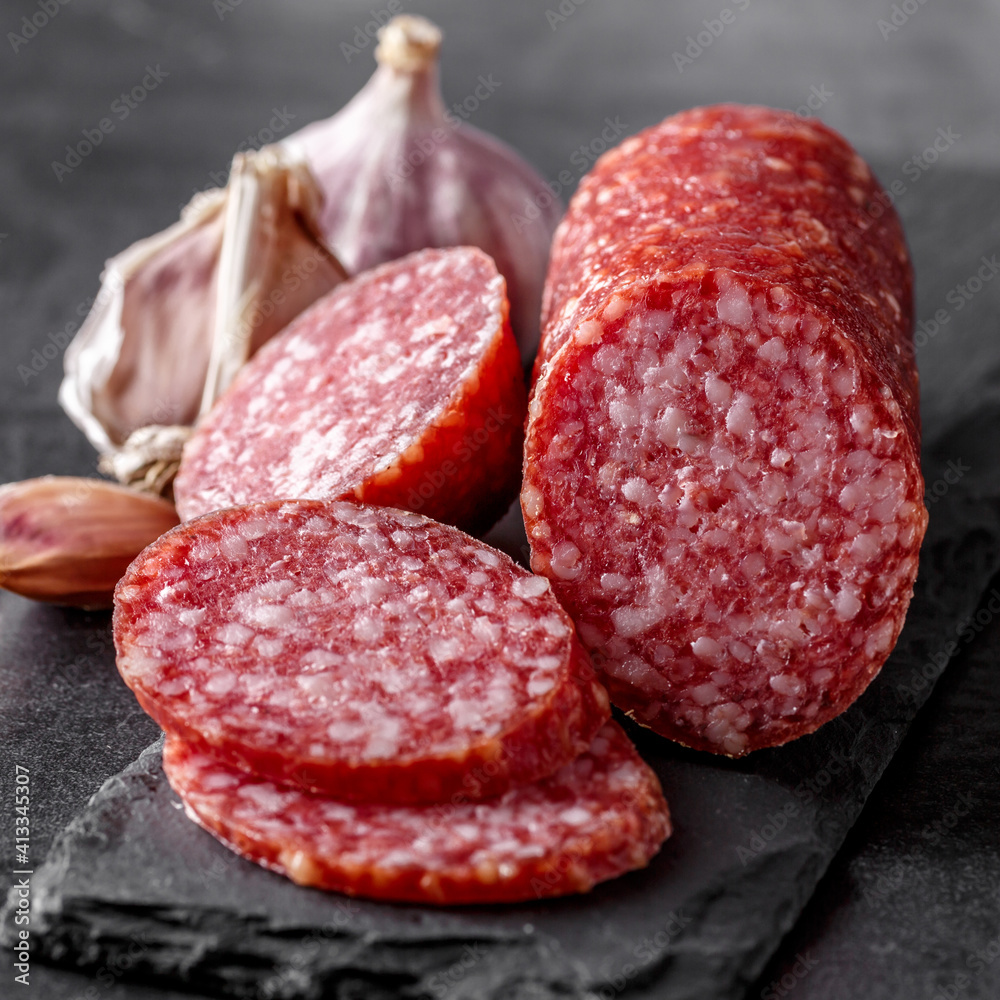 Traditional smoked salami sausage with spices.Salami sausage slices on a black chopping Board. Dark background. Traditional smoked salami sausage with spices.Salami sausage slices on a black chopping Board. Dark background.