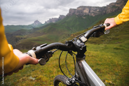 Close-up of a young woman cyclist holding the handlebars of her mountain bike against the backdrop of mountains and epic rocks. Focus on hand