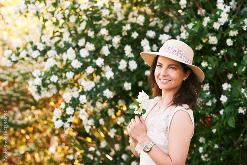 Outdoor portrait of beautiful mature woman in spring park enjoying blossoming of Jasmine flowers © annanahabed