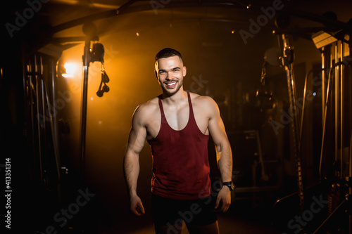 Muscular man smiles and shows the muscles of his body in the gym.