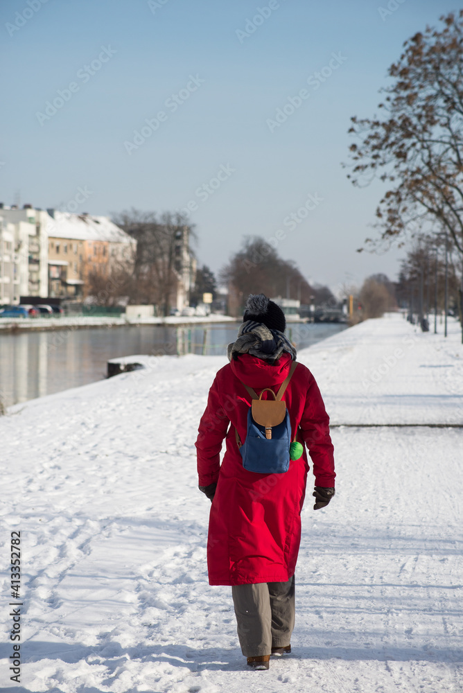 Portrait on back view of woman walking in border the frozen river wearing a winter red  coat