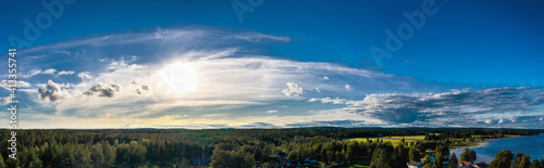 Breathtaking Aerial Panorama on Northern Scandinavian landscape with much pine tree and spruce forests. Big forest to horizon line, lake, bright Sun in blue scenic summer skies. Umea, Northern Sweden © Alexandre Patchine