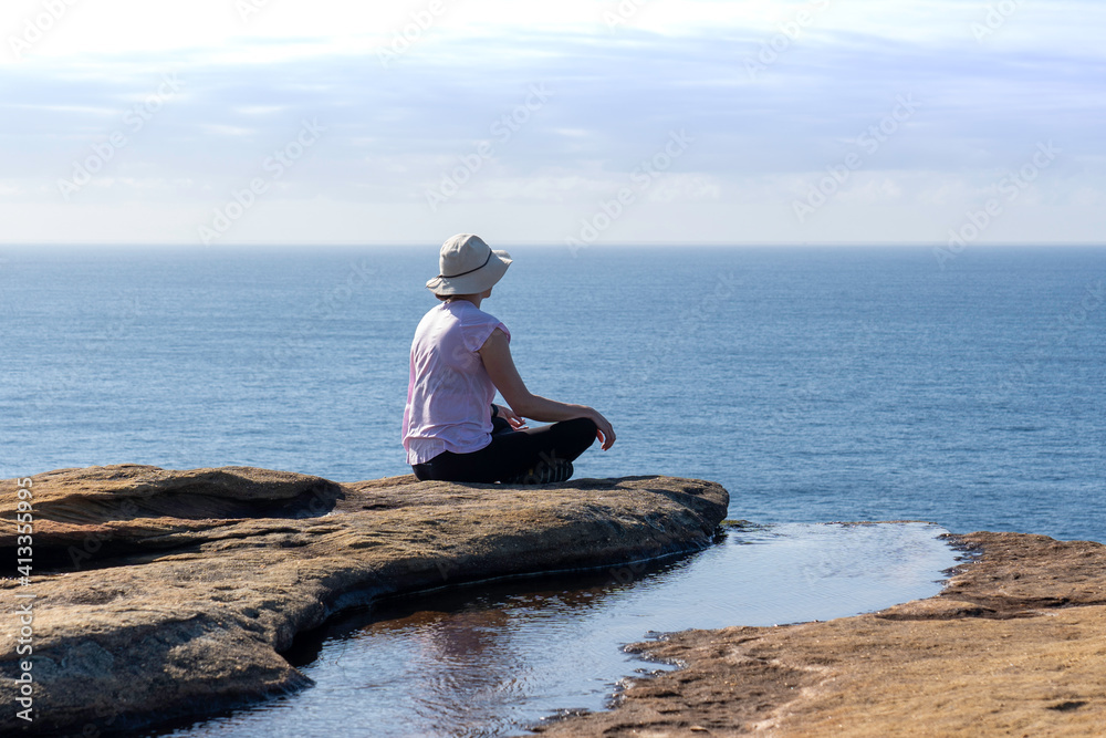 lady person sitting next to Rock pool on coastal cliff along coastline walk in the Royal National Park NSW, overlooking the ocean lady person sitting next to Rock pool on coastal cliff along coastline walk in the Royal National Park NSW, overlooking the ocean