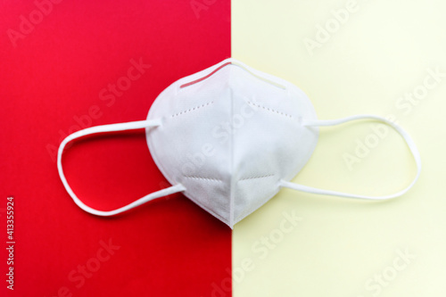 White mask FFP2, N95 on a red and yellow background. Medical respiratory mask against the virus, top view.