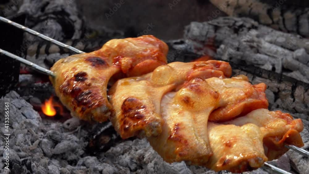 Mouth-watering chicken wings on the skewers are flipped above the coals outdoors in rapid footage Mouth-watering chicken wings on the skewers are flipped above the coals outdoors in rapid footage