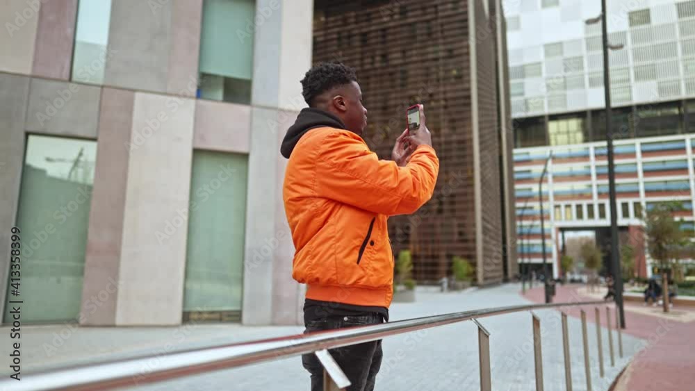 Stylish portrait of a cool black african american mobile photographer in a downtown city center. He takes photos of modern business buildings . Shot in 4k. City exploring