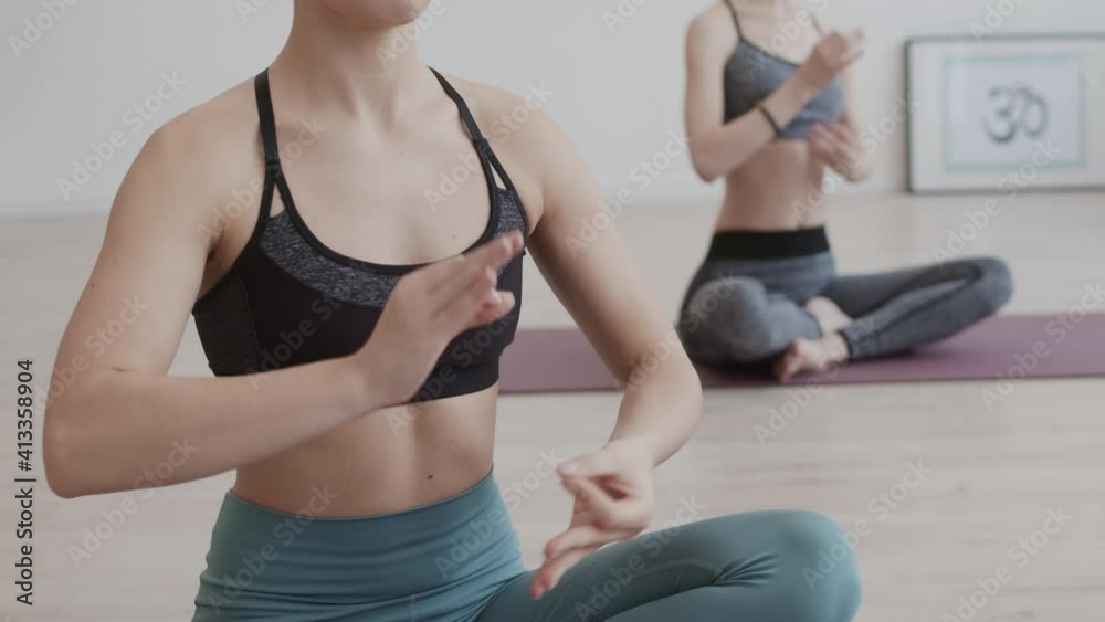Lockdown of pair of unrecognizable female yogi wearing trendy sport clothes sitting in cross-legged pose on yoga mats during yoga practice and meditating Lockdown of pair of unrecognizable female yogi wearing trendy sport clothes sitting in cross-legged pose on yoga mats during yoga practice and meditating