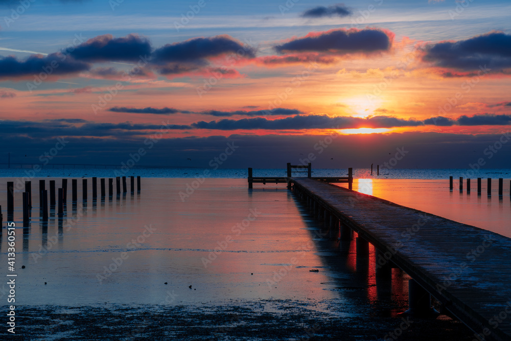Fototapeta premium Wooden jetty on sea with sunset in the background.