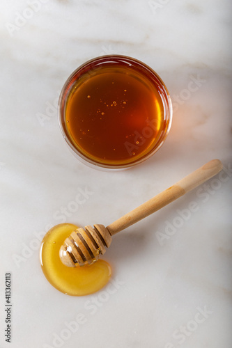 Glass jar full of honey and dipper. Honey in a glass jar with a stick on white marble. Top view.