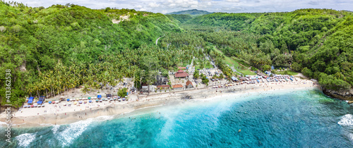 Magnificent aerial panorama of tropical beach at end of mountain valley with coconut palms, boats in blue water in Ocean gulf, unrecognized people, Crystal Bay beach, Nusa Penida, Bali, front view