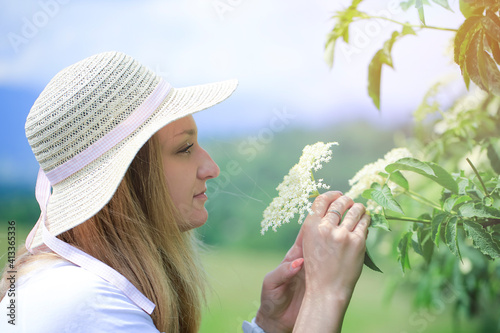 A young beautiful woman squeals the flowers of black elderflower (Sambucus nigra). photo