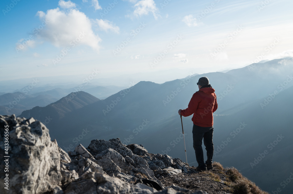 Young hiker Man standing with trekking poles on cliff edge and looking at Tatra mountains valley. Successful summit concept image.