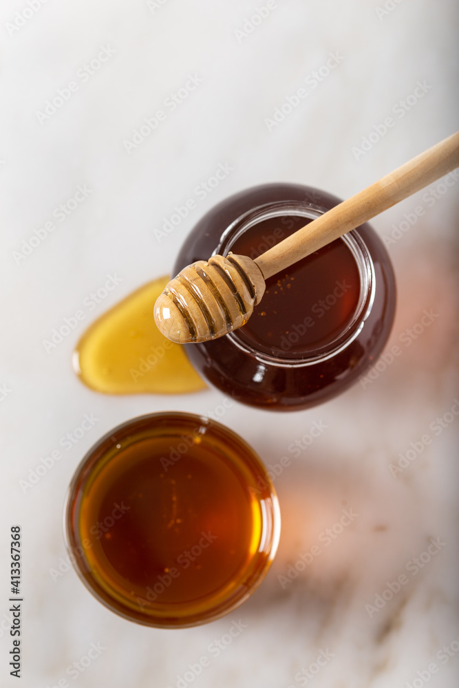 Glass jar full of honey and dipper. Honey in a glass jar with a stick on white marble. Top view. Glass jar full of honey and dipper. Honey in a glass jar with a stick on white marble. Top view.