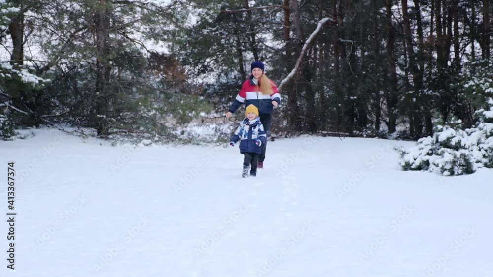 Positive happy blonde woman running through fluffy white snow with little boy, cute family having fun together playing in snowy forest enjoying winter, slow motion Positive happy blonde woman running through fluffy white snow with little boy, cute family having fun together playing in snowy forest enjoying winter, slow motion