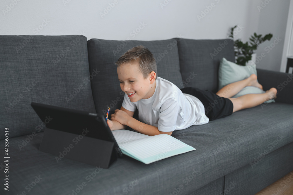 Online education, homeschooling. School boy having online lesson at home on the coach Online education, homeschooling. School boy having online lesson at home on the coach