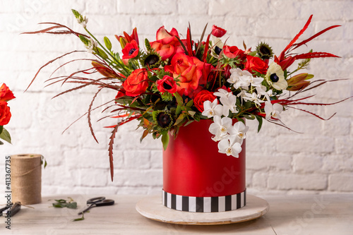 Floral arrangement in red shades of orchids, roses, sunflowers, lilies, alstroemerias and ornithogalums in a red box against a white brick wall. Professional florist work photo