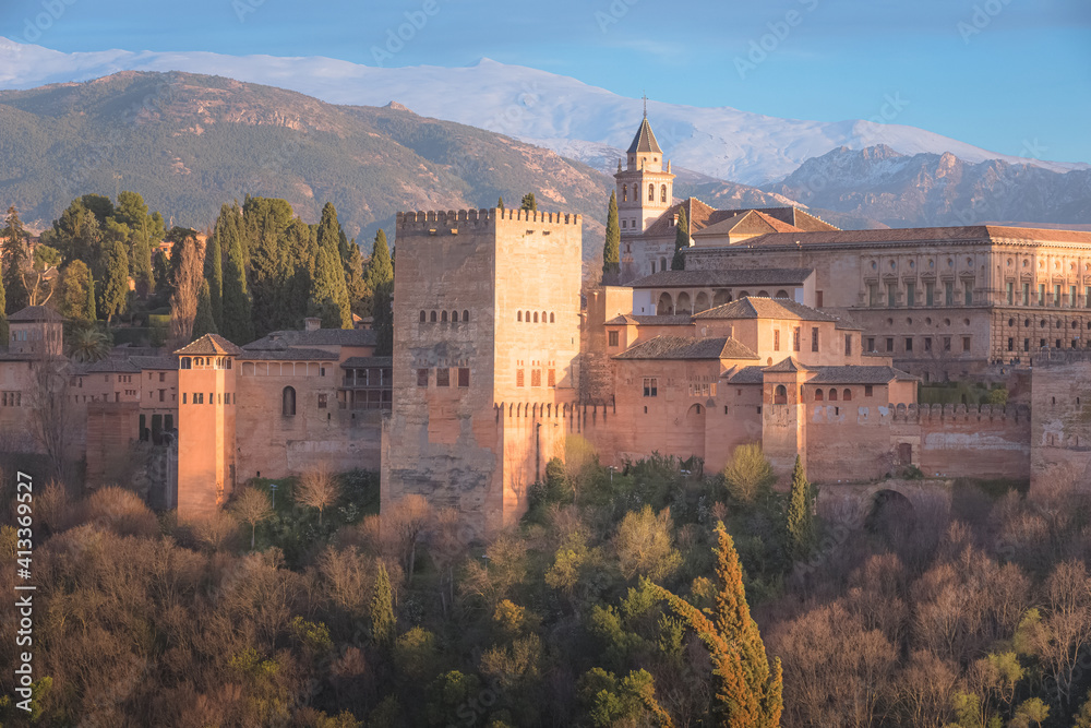 Classic view with sunset or sunrise golden light of Charles V Palace, the iconic Alhambra and Sierra Nevada Mountains from Mirador de San Nicolas in the albaicin old town of Granada, Andalusia, Spain.