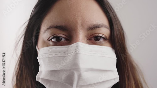 Close-up of a woman's face with mask looking at a serious camera indoors. photo