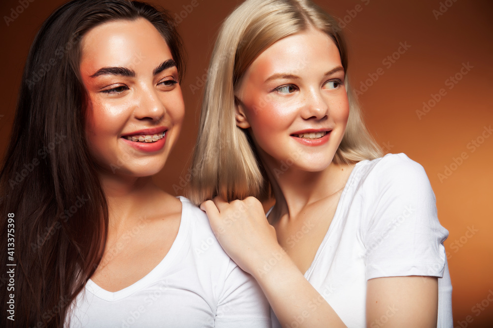 two pretty diverse girls happy posing together: blond and brunette, caucasian and asian on brown background, lifestyle people concept two pretty diverse girls happy posing together: blond and brunette, caucasian and asian on brown background, lifestyle people concept