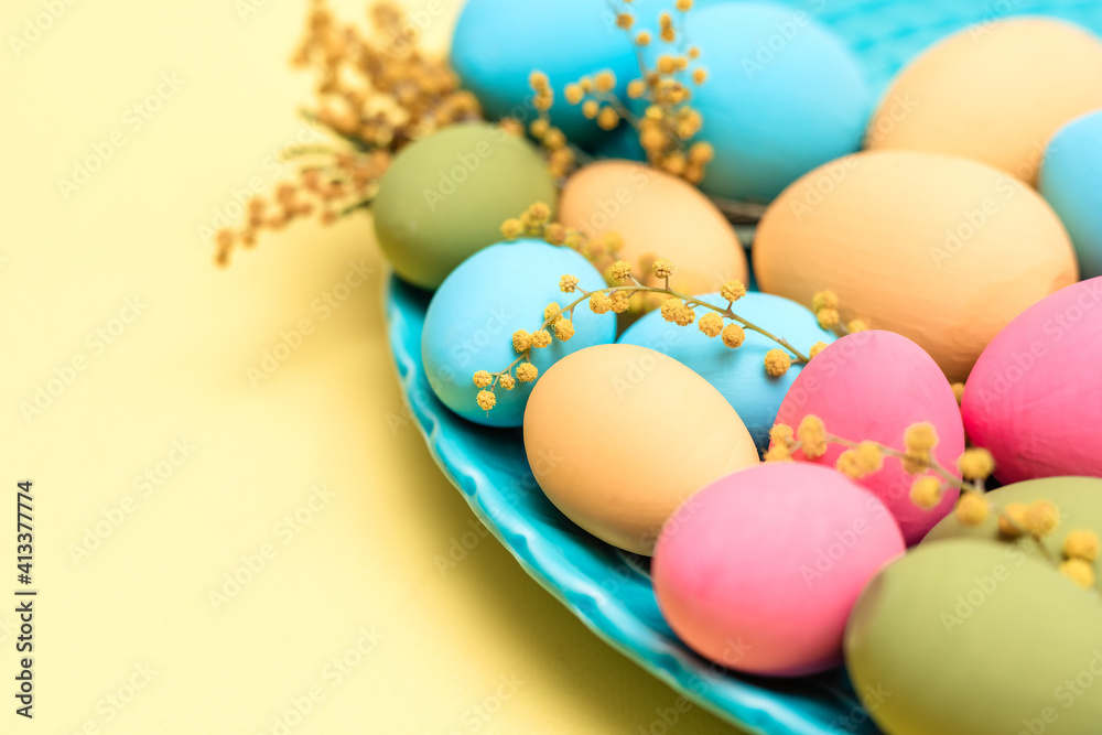 Turquois dish with painted blue, green, yellow, and pink eggs with mimosa