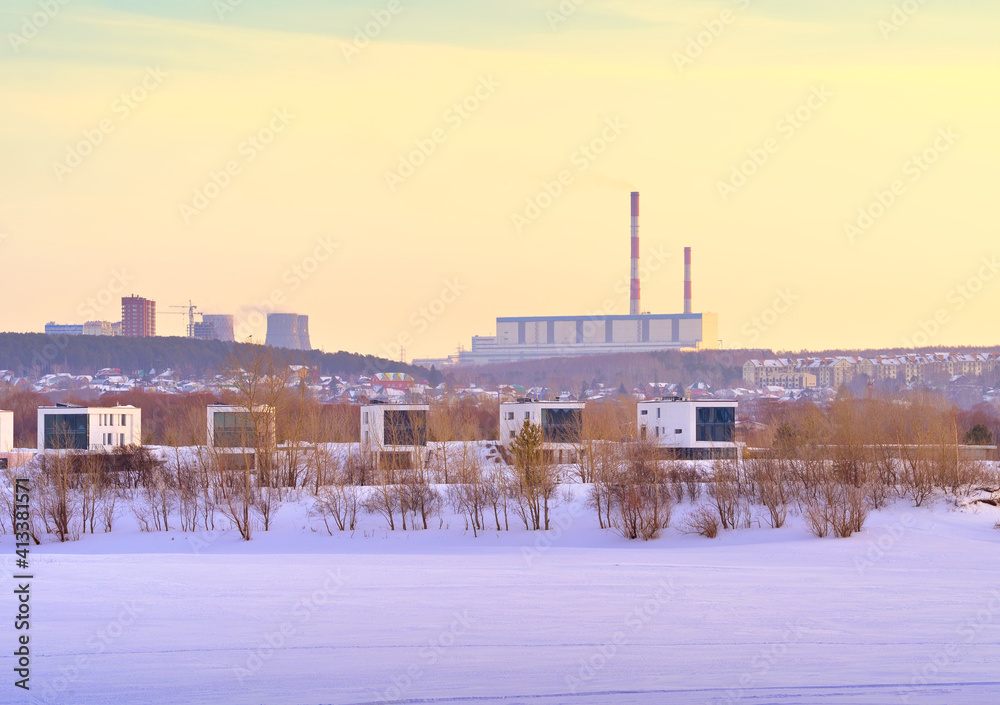 Winter morning on the Ob. New residential area on the frozen river bank in Novosibirsk, heat station pipes on the horizon