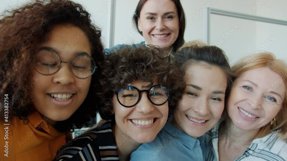 Slow motion portrait of funny women young and mature taking selfie making grimaces and looking at camera standing indoor in office having fun together.