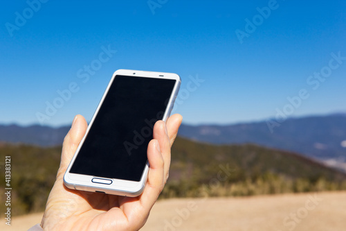 青空を背景にスマートフォンを持つ手	