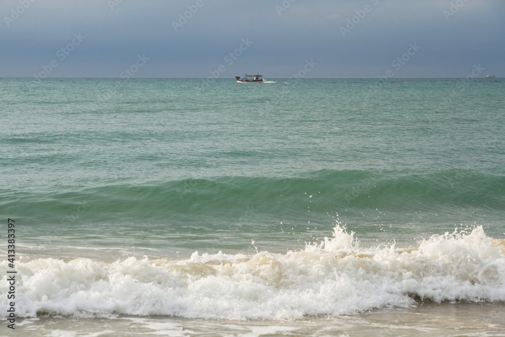 Fishing boat in the sea seen from the shore of the beach with waves coming 