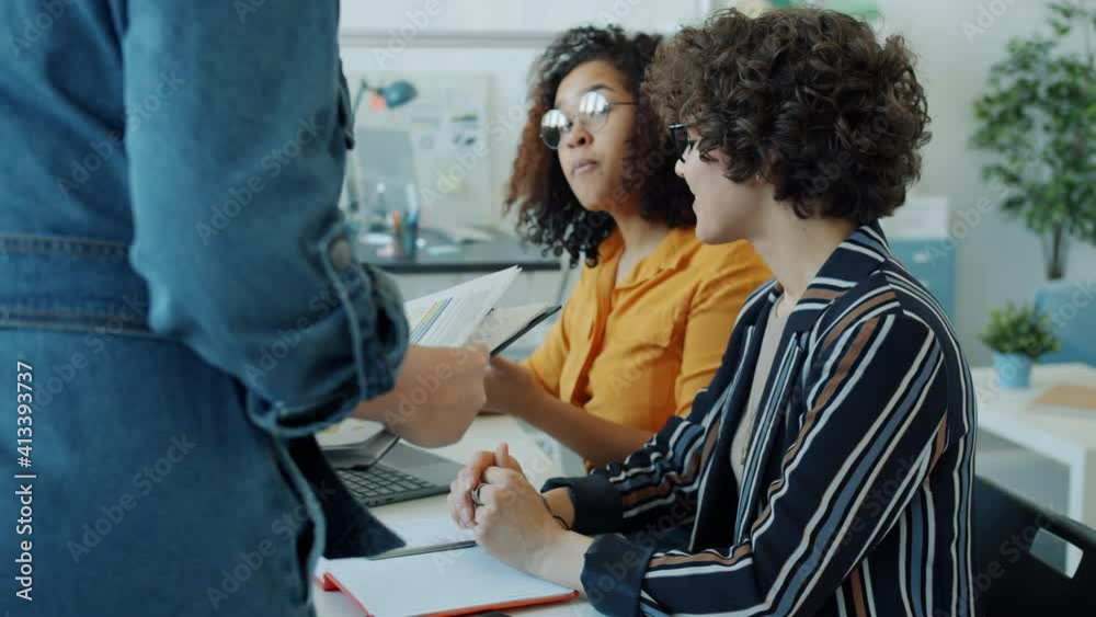 Female colleagues Caucasian and African American are talking looking at charts working in office together. Communication and business activities concept. Female colleagues Caucasian and African American are talking looking at charts working in office together. Communication and business activities concept.
