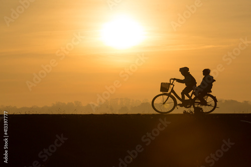 Asian kids riding the bicycle during the morning with the background of sunrise in summer. Both child feeling happiness with them lifestle to exercise before go to school