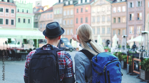 Back view of young tourists couple with bags checking map on central city square. They discussing their new destination.