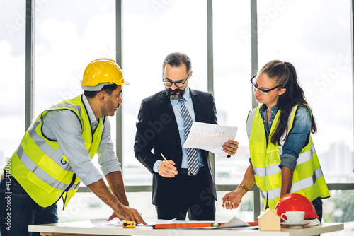 Professional of team engineers cargo foreman in helmets working with blueprint and construction tools on table at the construction site