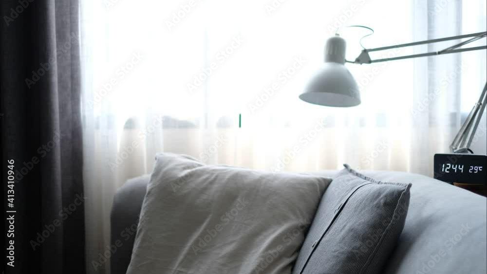 The sunlight shines through the large windows and the curtains descend on the gray sofas in the morning and there is a digital clock. Count the time beside timelapse