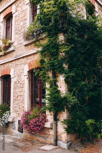 Facade of old stone buildings in Perouges, red windows, flowers, France © Lena Ivanova