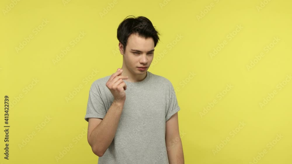 I need cash. Sly young man in casual style gray t-shirt showing money gesture and smiling, pretending to scattering money, planning to become rich. Indoor studio shot isolated on yellow background I need cash. Sly young man in casual style gray t-shirt showing money gesture and smiling, pretending to scattering money, planning to become rich. Indoor studio shot isolated on yellow background