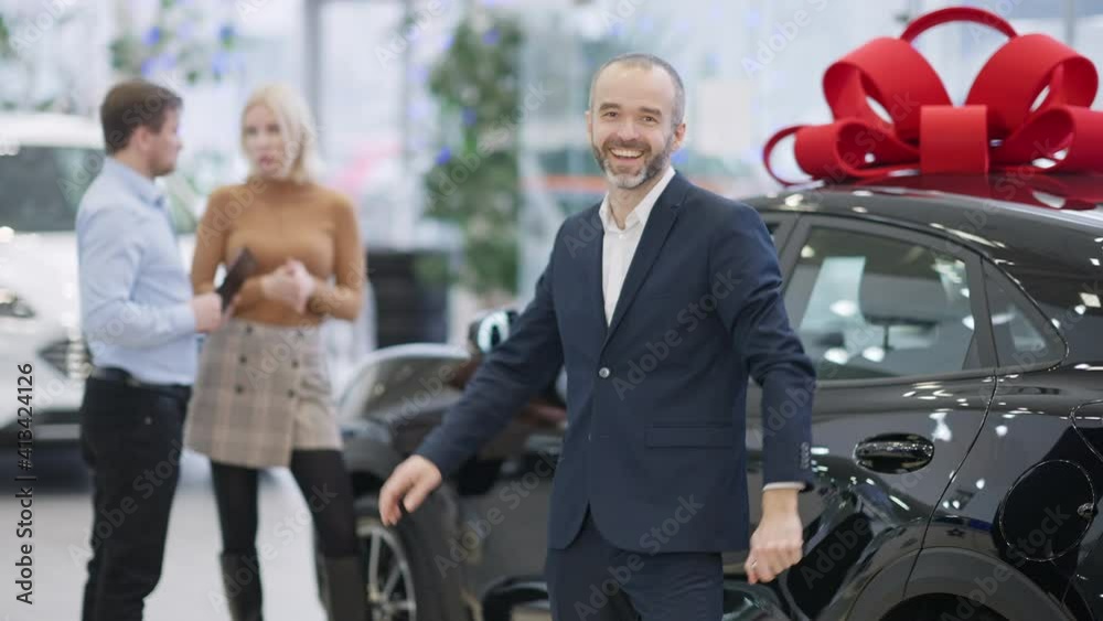 Excited bearded man stretching car keys to camera and laughing. Portrait of happy Caucasian businessman buying new automobile in dealership with employee consulting client at background. Excited bearded man stretching car keys to camera and laughing. Portrait of happy Caucasian businessman buying new automobile in dealership with employee consulting client at background.
