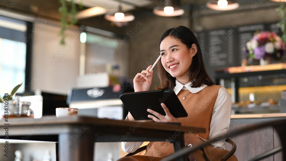 Smiling young female designer holding digital tablet and thinking about her project while sitting in modern office. Smiling young female designer holding digital tablet and thinking about her project while sitting in modern office.